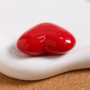 Macro shot of glossy red resin heart bead with thread hole on white porcelain plate