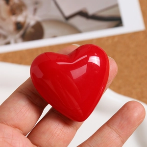 Close-up of a vibrant red polished heart-shaped charm pendant held in a person's hand