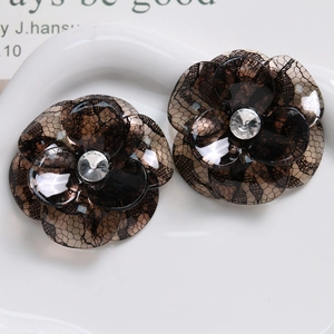 Close-up of translucent brown acetate camellia hair pins with black lace patterns and rhinestones