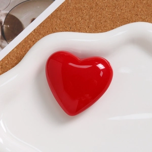 Macro shot of glossy red resin heart charm on a decorative white textured ceramic tray