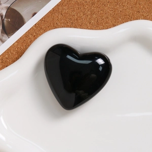 Close-up of a polished black heart-shaped stone charm on a white ceramic jewelry tray