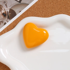 Macro shot of bright orange resin heart charm on a decorative white ceramic plate