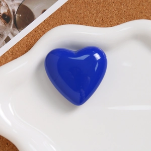 Macro detail of glossy blue heart-shaped resin accessory on a white ceramic plate