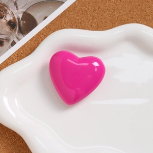 Close-up of a glossy rose pink heart-shaped pendant on a white ceramic plate