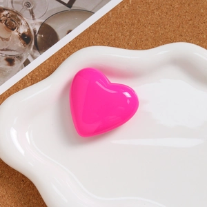 Macro view of a glossy pink heart-shaped pendant in a stylish white ceramic dish