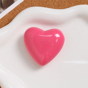 Macro shot of 3D glossy pink heart charm on a white ceramic plate and cork surface