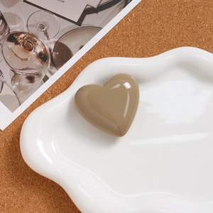 Detailed view of glossy taupe heart-shaped accessory on a white textured ceramic tray