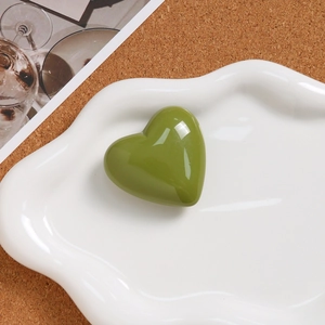 Macro shot of olive green heart pendant placed in a white cloud-shaped ceramic tray
