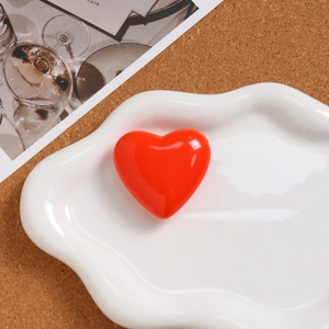 Close-up of a glossy red resin heart charm on a decorative white cloud ceramic tray