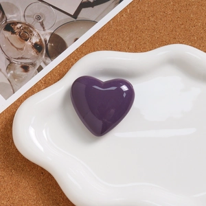Close-up of a polished purple heart pendant on a white ceramic tray with soft lighting