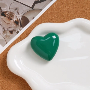 Macro shot of a glossy emerald green heart pendant resting on a white ceramic plate