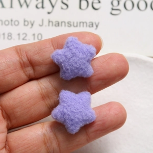 Macro view of small purple plush star accessories held between fingers for size reference