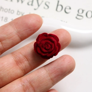 Close-up of a velvet burgundy rose flower bead for DIY jewelry being held by fingers