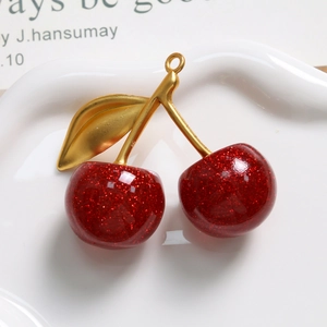 Makroaufnahme von glitzerndem Kirsch-Anhänger aus rotem Harz mit goldener Metallblatt