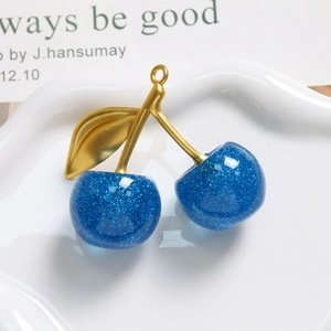 Details von blauem Glitzer-Kirsch-Anhänger mit Goldblatt auf weißem Schmucktablett