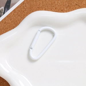 White D-ring carabiner in a ceramic cloud tray on cork background, minimalist aesthetic