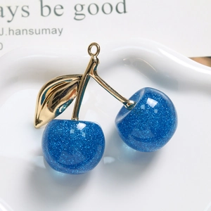 Makroaufnahme von blauem Glitzer-Kirsch-Anhänger mit goldenem Stiel auf weißem Teller