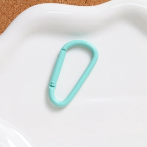 Close-up of mint green D-shaped aluminum spring hook on white ceramic tray