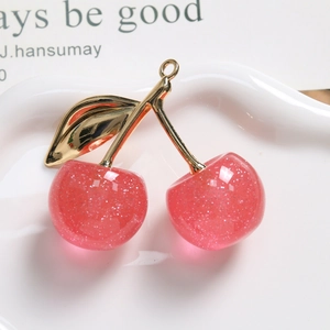 Makroaufnahme von glitzerndem rosa Kirsch-Anhänger mit goldenem Blatt und Aufhängeöse