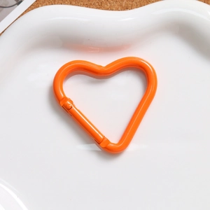 Orange heart-shaped alloy spring clasp for DIY keychains in a white ceramic dish
