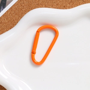 Close-up of orange pear-shaped aluminum spring carabiner on a decorative tray