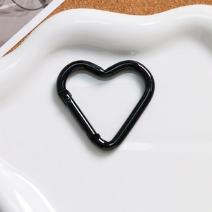 Glossy black heart-shaped carabiner hook with spring clip on white ceramic plate