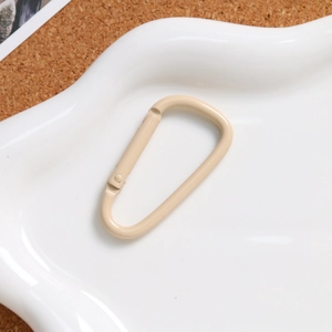 Detail of beige D-ring carabiner with matte finish on a textured white tray background