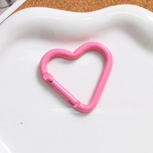 Macro shot of pink heart-shaped alloy spring clasp on a matching white ceramic plate
