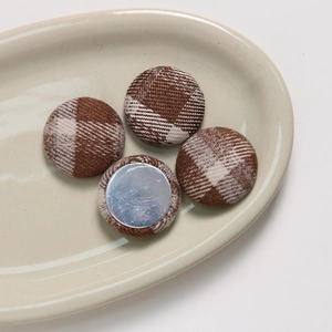 Macro view of plaid fabric covered buttons and smooth metal back on ceramic tray