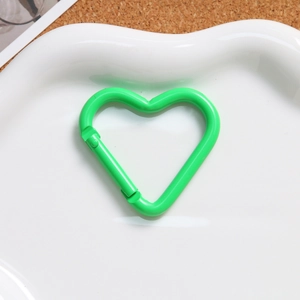 Macro shot of bright green heart-shaped alloy spring clasp on a white ceramic plate