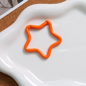 Detail of an orange star-shaped spring buckle on a white tray with cork background