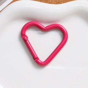 Close-up of rose pink heart-shaped carabiner alloy spring hook in a ceramic dish