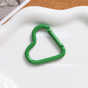 Macro shot of green heart-shaped aluminum spring hook on a white cloud tray