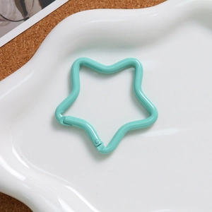 Macro view of a mint green star shaped alloy spring clasp on a white wavy ceramic plate