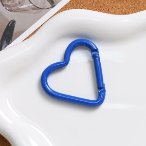 Close-up of a heart-shaped blue carabiner with spring gate on a white decorative tray