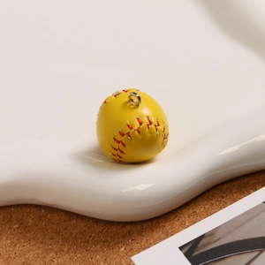 Macro shot of yellow mini baseball keychain with realistic texture and red hand stitching