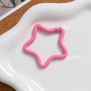 Macro detail of pink star-shaped alloy spring clasp on a white wavy tray background