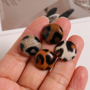 Detail shot of four round leopard print fabric buttons held by hand for scale