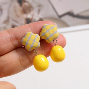 Macro detail of plaid fabric flower stud earrings with yellow bean drops held in hand