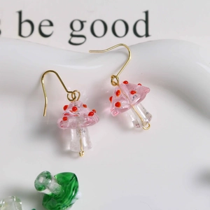 Macro shot of handmade pink glass mushroom earrings with red dots and golden hooks
