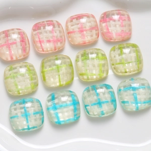 Close-up of square resin cabochons with colorful woven grid patterns on a white plate