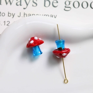 Detail of red polka dot glass mushroom bead with translucent blue stem and gold pin