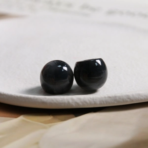 Macro shot of polished black resin spherical beads on a white textured tray for DIY jewelry