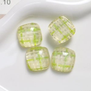 Macro view of square resin DIY charms with green and white plaid patterns on a ceramic plate