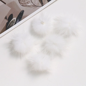 Detail shot of five soft white fluffy faux fur pompoms for DIY craft accessories