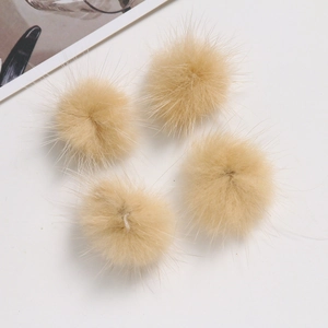 Close-up of four light brown faux mink fur pom poms for DIY crafts and accessories