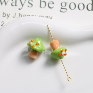 Macro shot of green glass mushroom beads with orange dots and gold metal pins for DIY jewelry