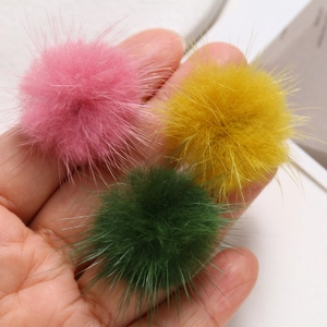 Close-up of 3.5cm fluffy mink fur pompoms in pink yellow and green on a hand