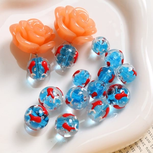 Vue détaillée de perles en verre de 12mm avec motifs de poissons et clous de roses