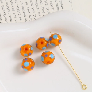 Macro shot of 10mm orange glass beads with blue dots and gold pin for DIY jewelry